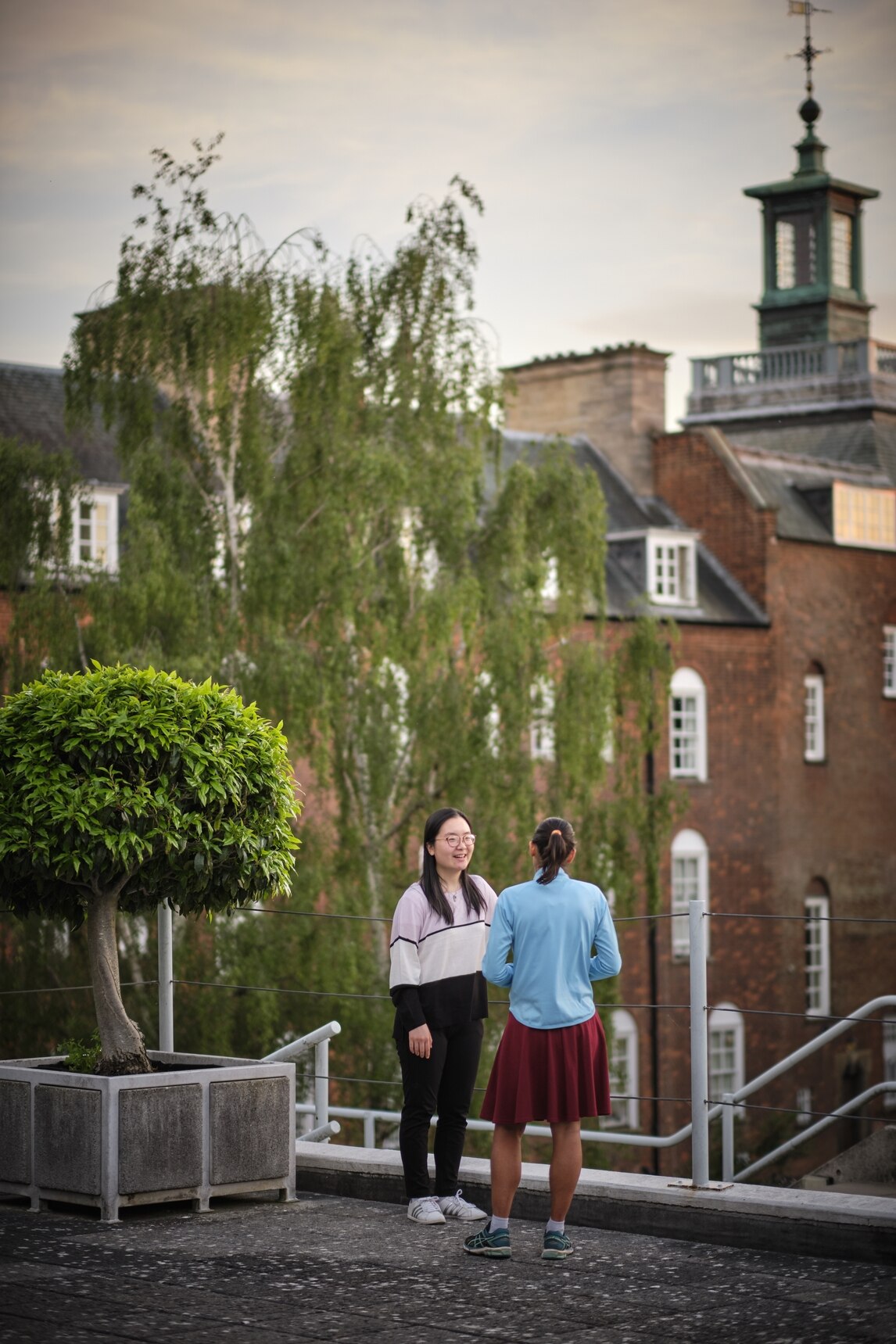 Two females chatting. Red brick building in background